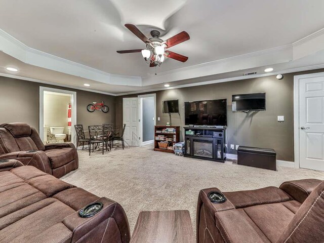 carpeted living room featuring a fireplace, a tray ceiling, ceiling fan, and ornamental molding