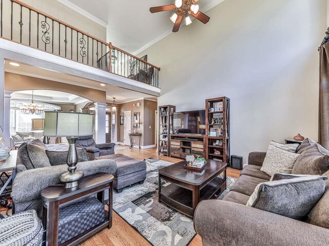 living room with a high ceiling, ceiling fan with notable chandelier, ornate columns, ornamental molding, and light hardwood / wood-style floors