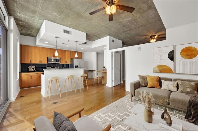 living room with visible vents, light wood-style floors, and a ceiling fan