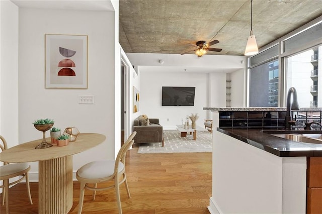 kitchen with a ceiling fan, light wood-style flooring, a sink, pendant lighting, and dark countertops