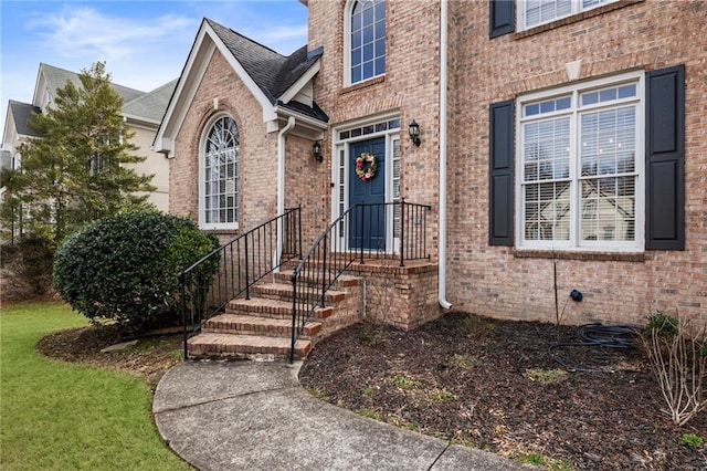 entrance to property featuring brick siding and a lawn