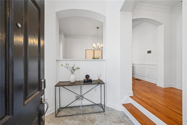 foyer featuring arched walkways, ornamental molding, light wood-type flooring, a chandelier, and a decorative wall