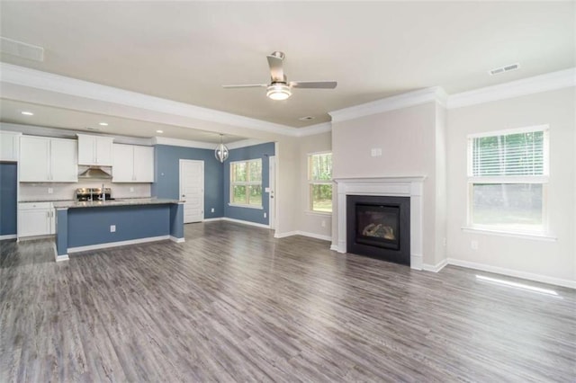 unfurnished living room with ornamental molding, dark wood-type flooring, ceiling fan, baseboards, and a glass covered fireplace
