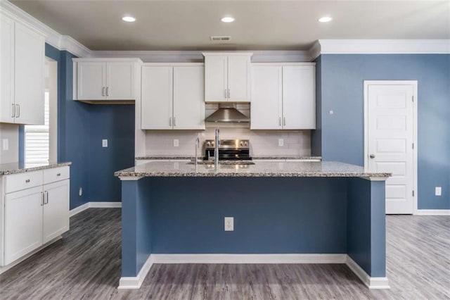 kitchen with wall chimney range hood, white cabinets, light stone countertops, ornamental molding, and recessed lighting