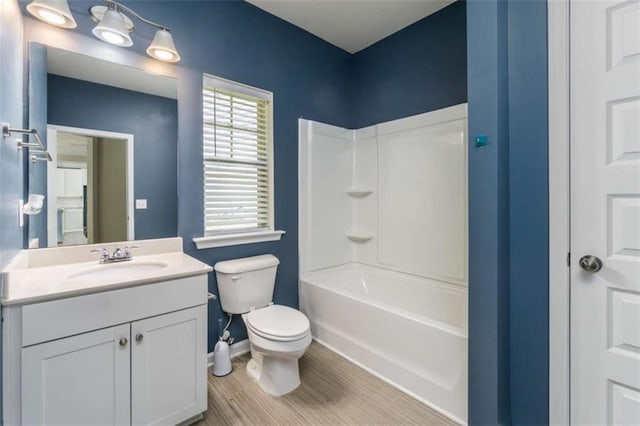 bathroom featuring baseboards, vanity, toilet, wood finished floors, and bathtub / shower combination