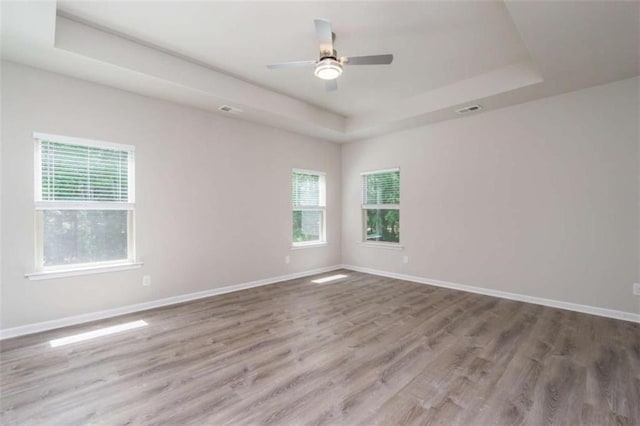 unfurnished room featuring a tray ceiling, healthy amount of natural light, wood finished floors, and baseboards