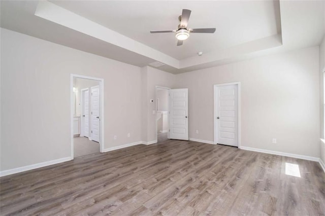 unfurnished bedroom with a raised ceiling, wood finished floors, baseboards, and ensuite bath