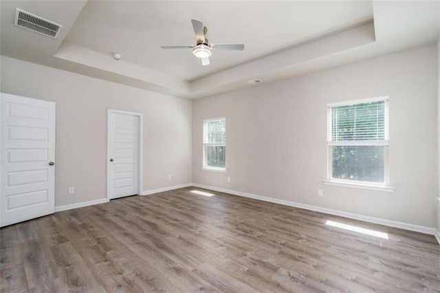unfurnished bedroom featuring a raised ceiling, multiple windows, wood finished floors, and baseboards