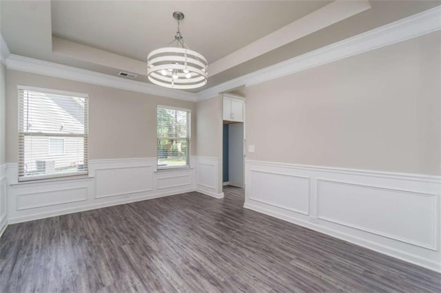 spare room featuring a raised ceiling, a chandelier, a wainscoted wall, ornamental molding, and dark wood-style floors