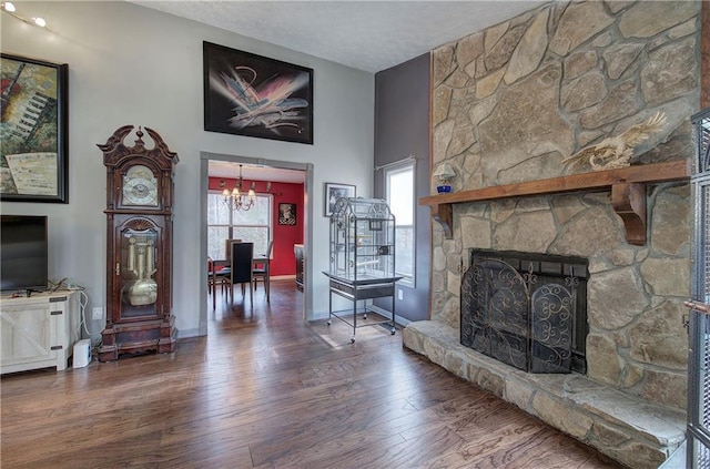 living room with dark wood-type flooring, an inviting chandelier, a textured ceiling, and a stone fireplace