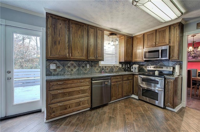 kitchen with appliances with stainless steel finishes, a notable chandelier, dark stone counters, dark hardwood / wood-style floors, and decorative light fixtures