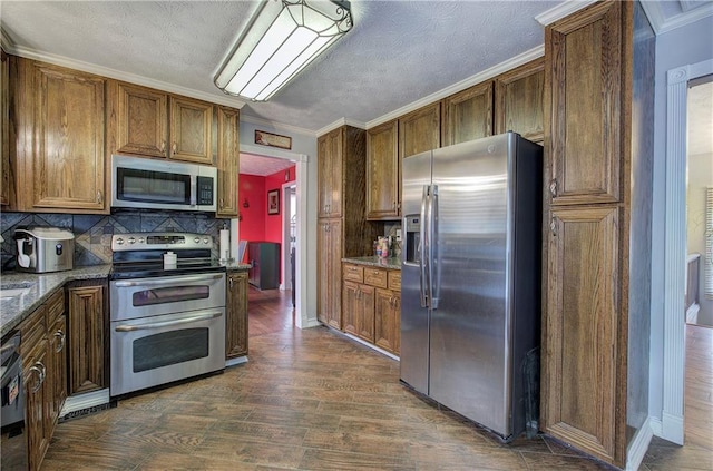 kitchen with dark stone countertops, backsplash, crown molding, stainless steel appliances, and dark hardwood / wood-style flooring