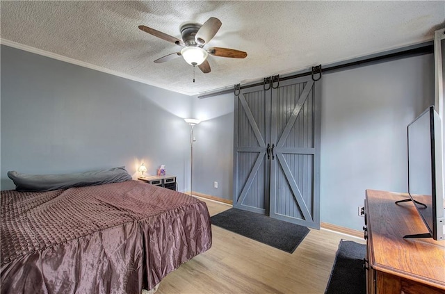 bedroom with a barn door, crown molding, a textured ceiling, and light hardwood / wood-style flooring