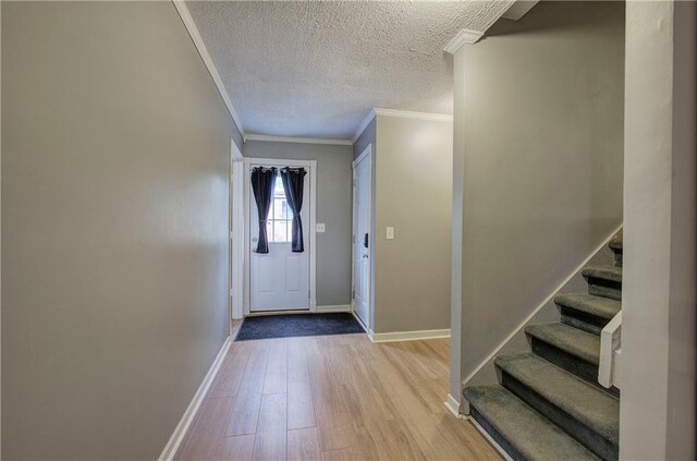 doorway with a textured ceiling, crown molding, and light hardwood / wood-style floors