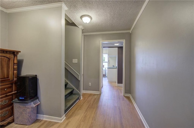 hallway with light hardwood / wood-style floors, a textured ceiling, and ornamental molding