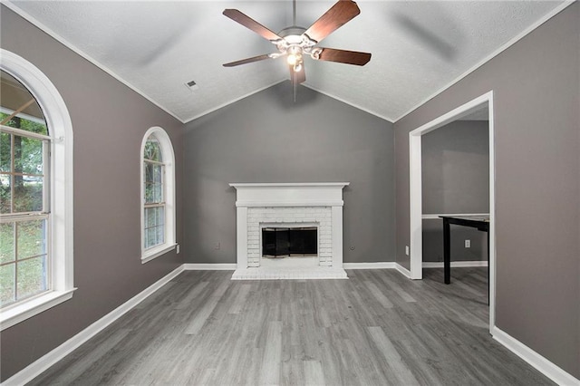 unfurnished living room with lofted ceiling, a brick fireplace, ceiling fan, a wealth of natural light, and wood-type flooring