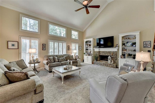 carpeted living room with ceiling fan, high vaulted ceiling, crown molding, and a stone fireplace