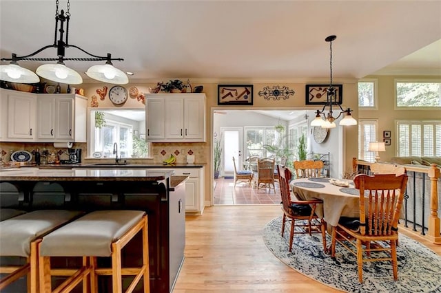 kitchen with tasteful backsplash, hanging light fixtures, white cabinetry, ornamental molding, and light hardwood / wood-style floors