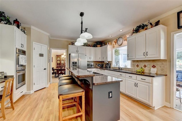 kitchen with white cabinets, hanging light fixtures, a breakfast bar area, appliances with stainless steel finishes, and a center island