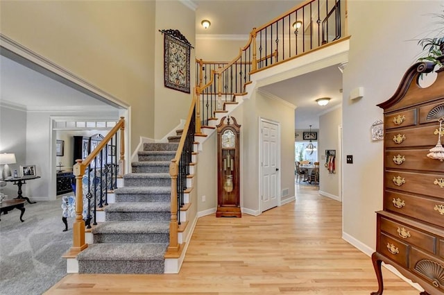 stairs featuring a towering ceiling, crown molding, and hardwood / wood-style floors