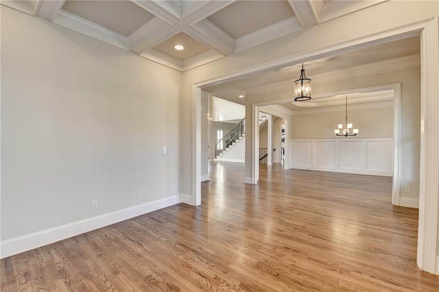 spare room with coffered ceiling, ornamental molding, light wood-type flooring, a chandelier, and beam ceiling