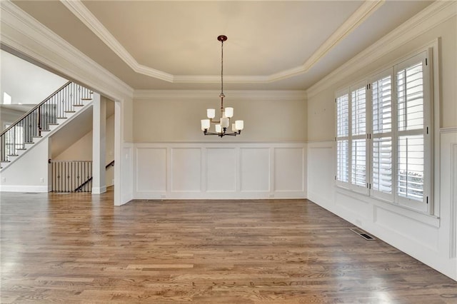 unfurnished dining area featuring a tray ceiling, visible vents, a decorative wall, an inviting chandelier, and wood finished floors