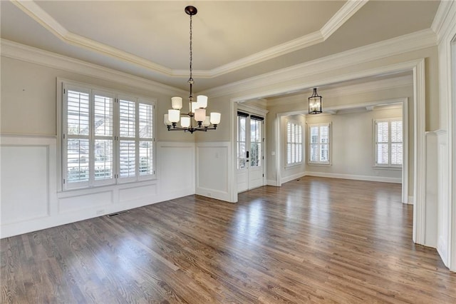 unfurnished dining area featuring a notable chandelier, a decorative wall, wood finished floors, visible vents, and ornamental molding