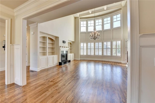 unfurnished living room featuring a glass covered fireplace, crown molding, an inviting chandelier, and wood finished floors