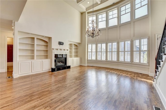 unfurnished living room featuring a chandelier, wood finished floors, a towering ceiling, a high end fireplace, and stairs