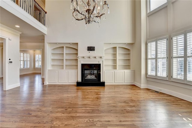 unfurnished living room featuring wood finished floors, a glass covered fireplace, and a towering ceiling