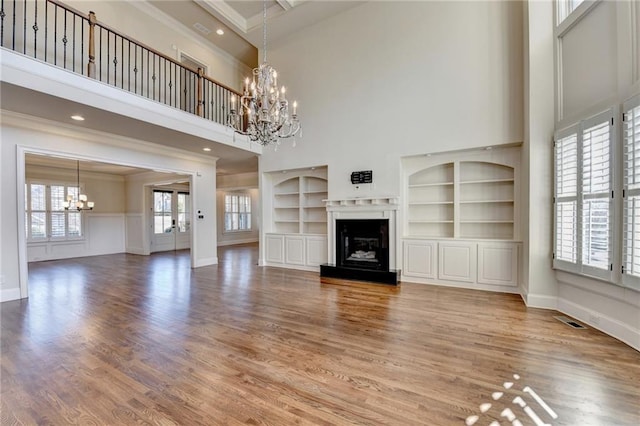 unfurnished living room featuring a chandelier, a fireplace with raised hearth, light wood-style flooring, visible vents, and crown molding