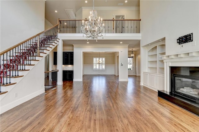 unfurnished living room featuring a chandelier, wood finished floors, a glass covered fireplace, and ornamental molding