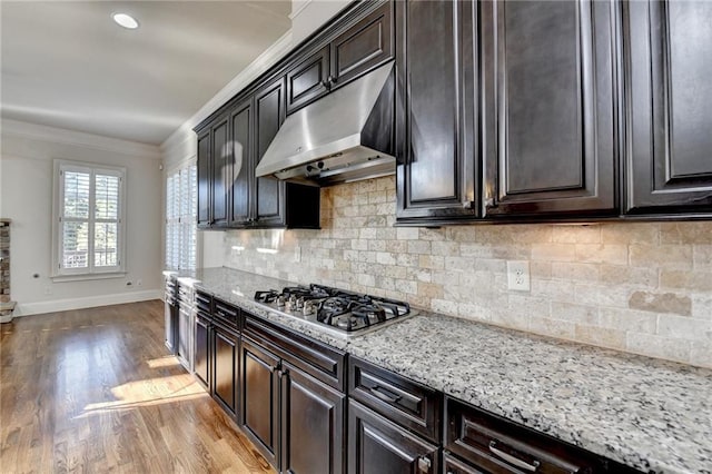 kitchen with light stone counters, wood finished floors, crown molding, under cabinet range hood, and stainless steel gas cooktop