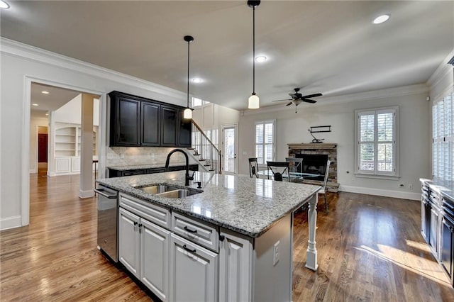 kitchen featuring dark wood finished floors, a center island with sink, ornamental molding, a sink, and a stone fireplace