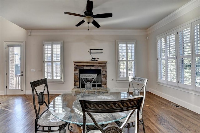 dining space featuring ornamental molding, a stone fireplace, wood finished floors, and a wealth of natural light