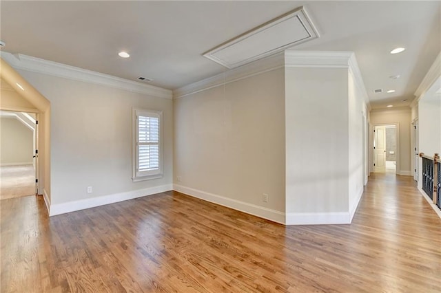 unfurnished room with attic access, visible vents, baseboards, ornamental molding, and light wood-style floors