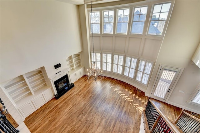 unfurnished living room with light wood-type flooring, built in features, a notable chandelier, and a glass covered fireplace