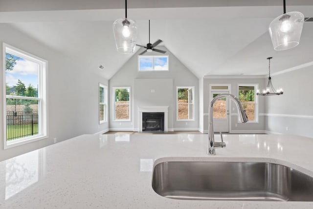 kitchen with pendant lighting, ceiling fan with notable chandelier, light stone counters, and sink