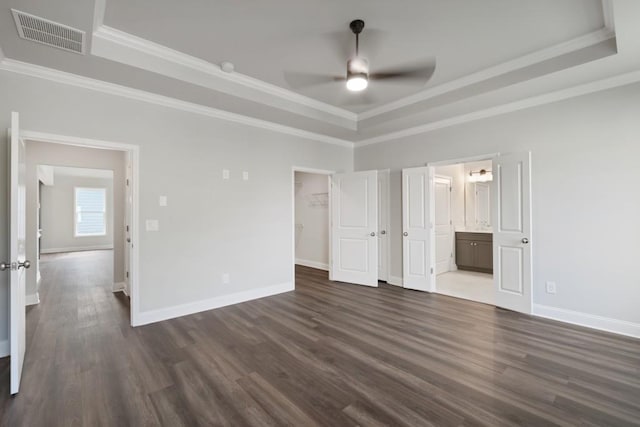 unfurnished bedroom featuring ensuite bathroom, a tray ceiling, ceiling fan, crown molding, and dark hardwood / wood-style floors