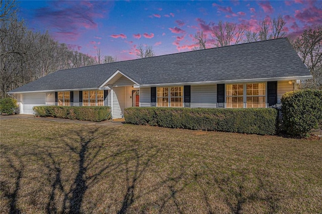 ranch-style home with a garage, roof with shingles, and a front lawn