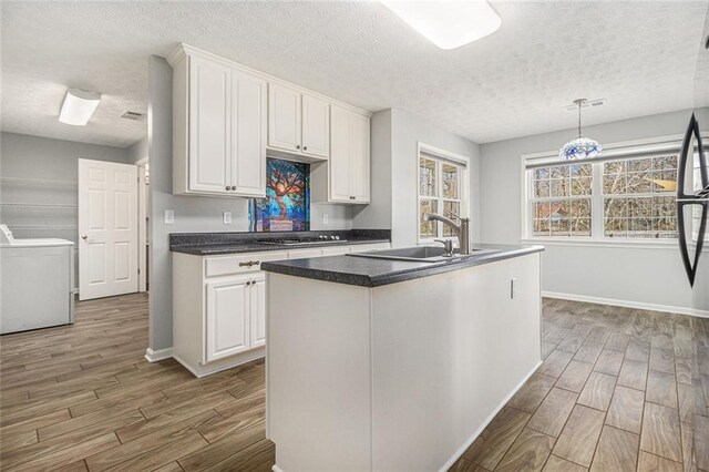 kitchen featuring a sink, wood finish floors, washing machine and dryer, and white cabinets