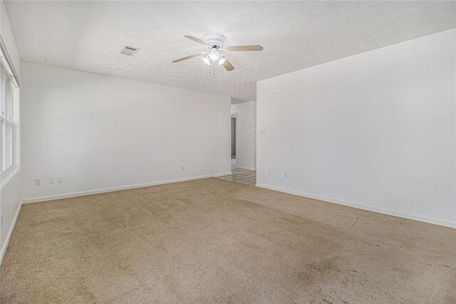 spare room with visible vents, a ceiling fan, light carpet, a textured ceiling, and baseboards