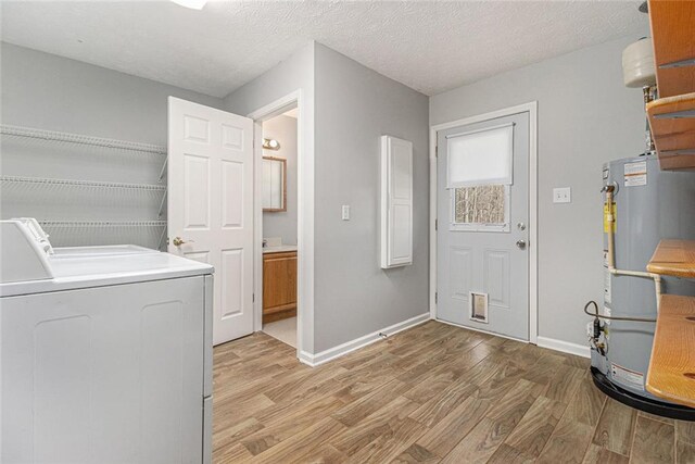 clothes washing area with laundry area, separate washer and dryer, baseboards, water heater, and light wood-style floors