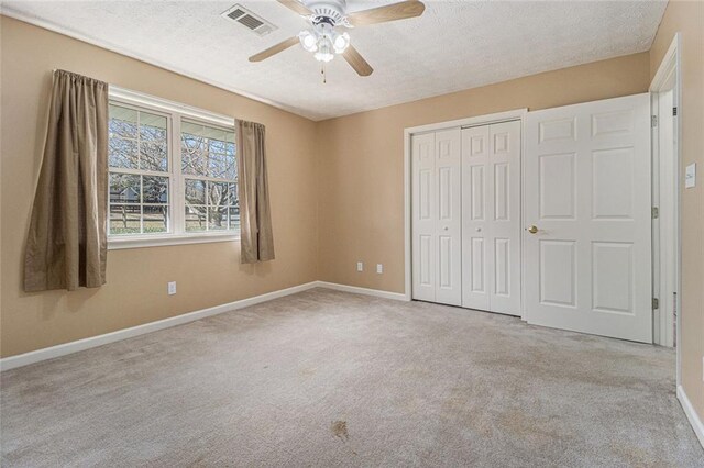 unfurnished bedroom with a textured ceiling, carpet flooring, visible vents, baseboards, and a closet