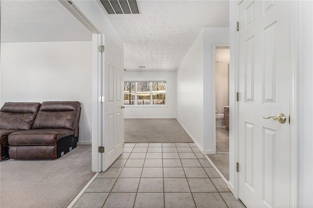 hallway with light tile patterned floors, a textured ceiling, light carpet, visible vents, and baseboards