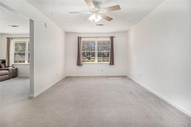 carpeted empty room with visible vents, ceiling fan, a textured ceiling, and baseboards