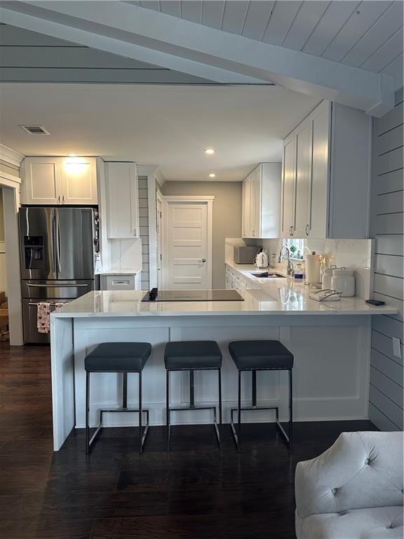 kitchen featuring a breakfast bar area, tasteful backsplash, stainless steel fridge with ice dispenser, beam ceiling, and white cabinets