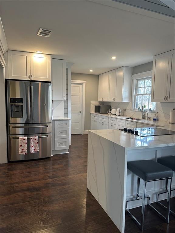 kitchen featuring stainless steel refrigerator with ice dispenser, dark wood-type flooring, a kitchen bar, white cabinetry, and tasteful backsplash