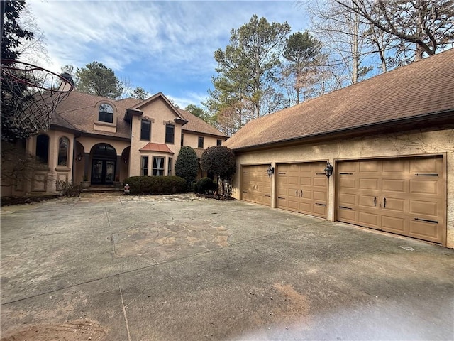 view of front facade featuring a garage, a shingled roof, and stucco siding