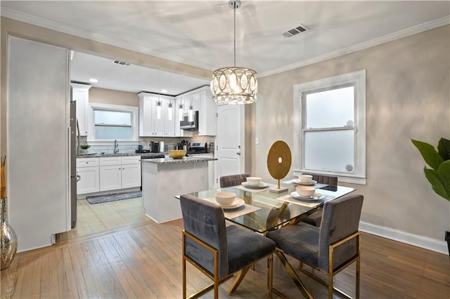 dining space featuring ornamental molding, light wood-type flooring, baseboards, and an inviting chandelier